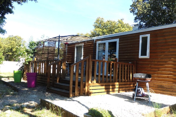 A wooden cabin with a porch, a grill, and a small deck.