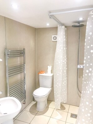 A bathroom with a toilet, a shower, a towel rack, and a sink. - Brewery Lodge Sleeps 4 (Blakeney)