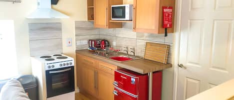 A compact kitchen with a stove, microwave, sink, and a red refrigerator.