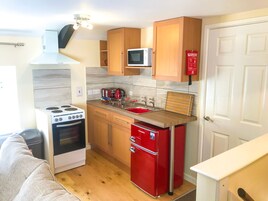 Una cocina compacta con estufa, microondas, pileta y un refrigerador rojo.