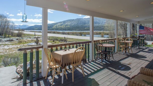 Eine überdachte Terrasse im Freien mit Tischen und Stühlen, mit Blick auf eine malerische Landschaft mit Bergen und einem Gewässer.