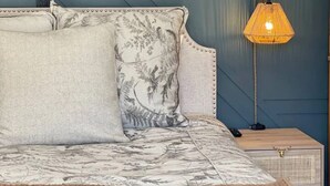 Ein Bett mit einem gemusterten Überwurf, zwei Kissen, einer Nachttischlampe und einem Nachttisch.