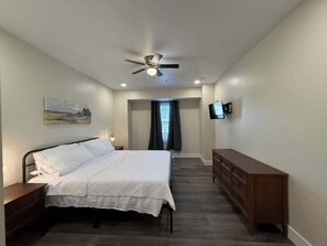 A bedroom with a bed, a dresser, a ceiling fan, a TV, and a painting on the wall. - Willow Creek Townhouse (Aliquippa)
