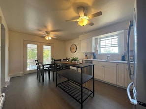 A kitchen with a dining table, chairs, ceiling fans, a clock, and a refrigerator.