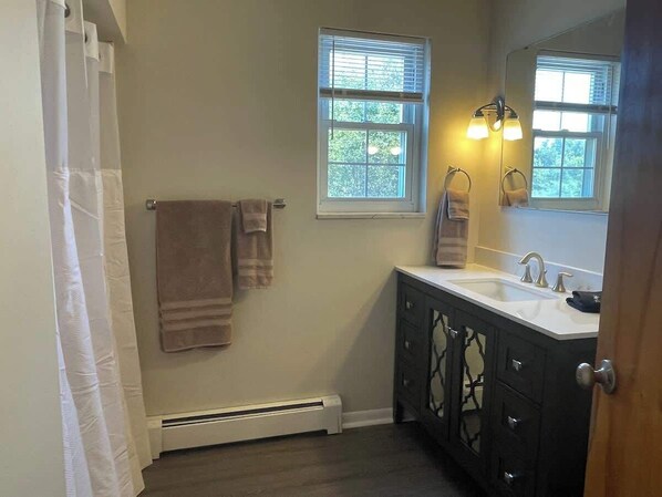 A bathroom with a white radiator, two windows with blinds, a sink with a mirror, and a towel rack with towels. - Cozy Colonial Retreat (Monaca)