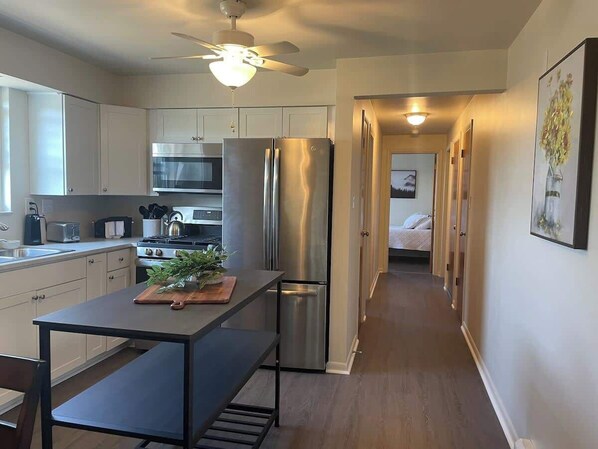 A modern kitchen with stainless steel appliances, a wooden island, and a ceiling fan.