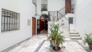 A clean, well-lit hallway with a marble floor, a staircase, and potted plants. - GuestReady - Atico Luna Puerto (El Puerto de Santa María)