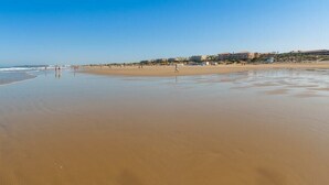 A wide sandy beach with a clear sky, a few people, and buildings in the background. - GuestReady - Atico Luna Puerto (El Puerto de Santa María)