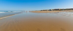 A wide sandy beach with a clear sky, a few people, and buildings in the background. - GuestReady - Atico Luna Puerto (El Puerto de Santa María)