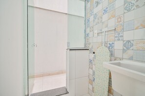 Casa de banho com chuveiro, lavatório e parede revestida a azulejos.