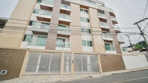 Um edifício residencial com vários andares, varandas, entrada com portão e linhas de energia visíveis.