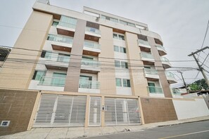 Um edifício residencial com vários andares, varandas, entrada com portão e linhas de energia visíveis.