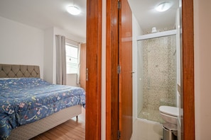 Quarto com cama, porta de madeira e área de chuveiro.