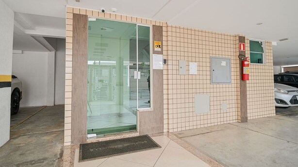 Uma entrada limpa e moderna com porta de vidro, paredes azulejadas, um extintor de incêndio e um carro estacionado do lado de fora.