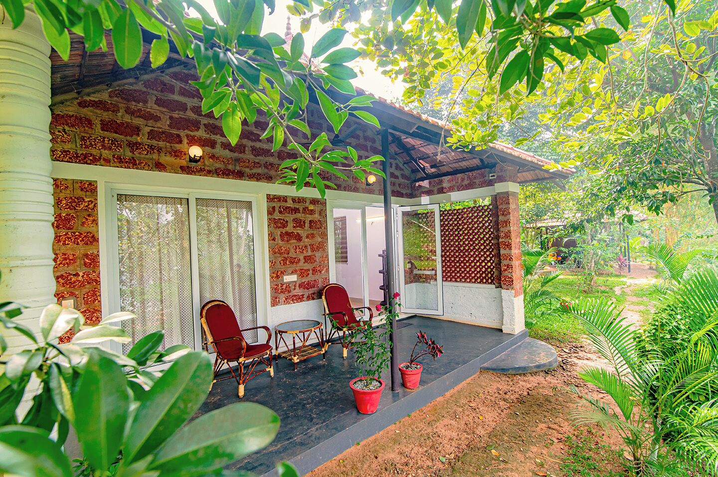A covered porch with two wicker chairs, a small table, and potted plants.