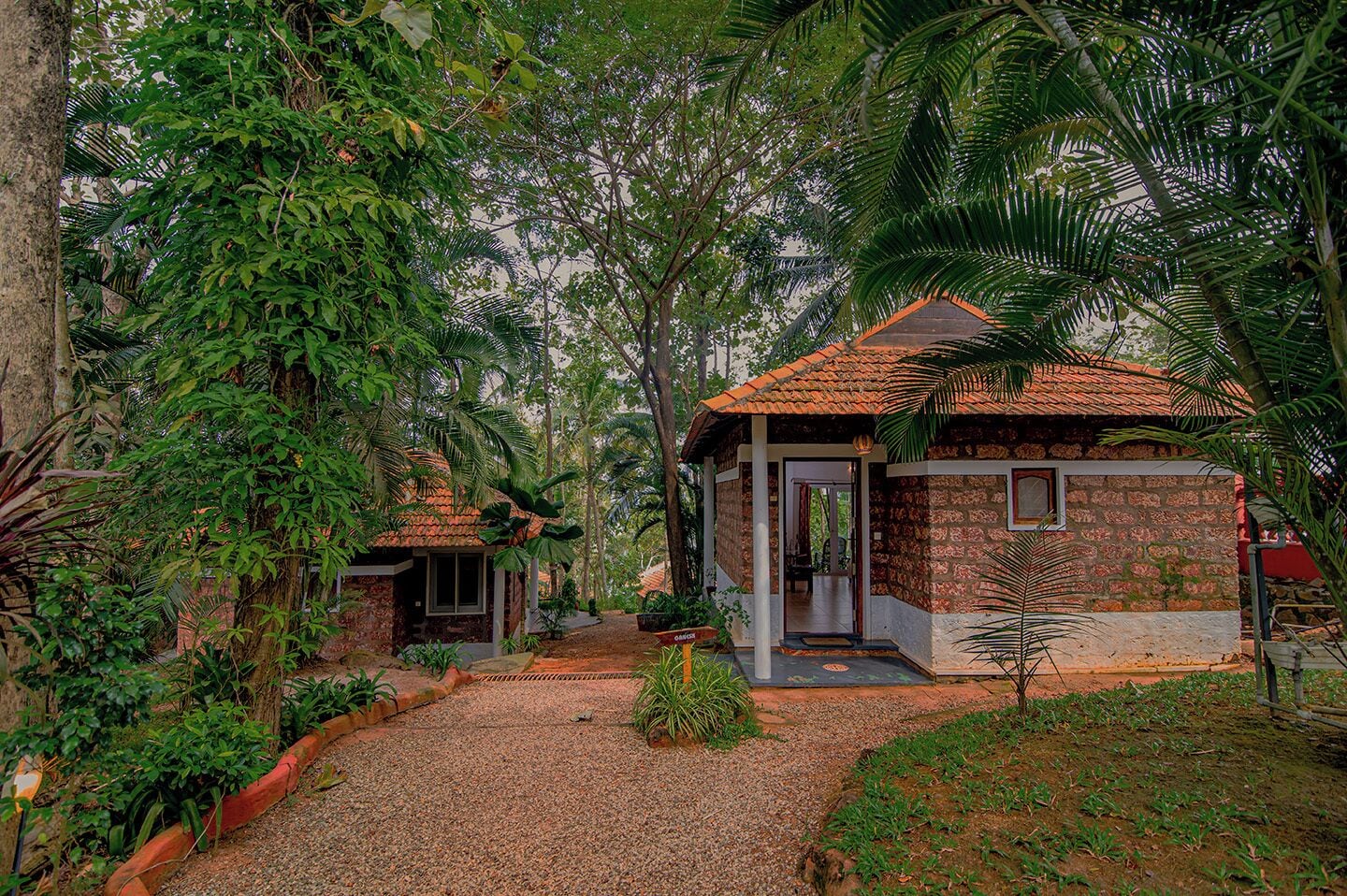 Une maison rustique, dotée d’un toit en tuiles, entourée d’une végétation tropicale luxuriante.