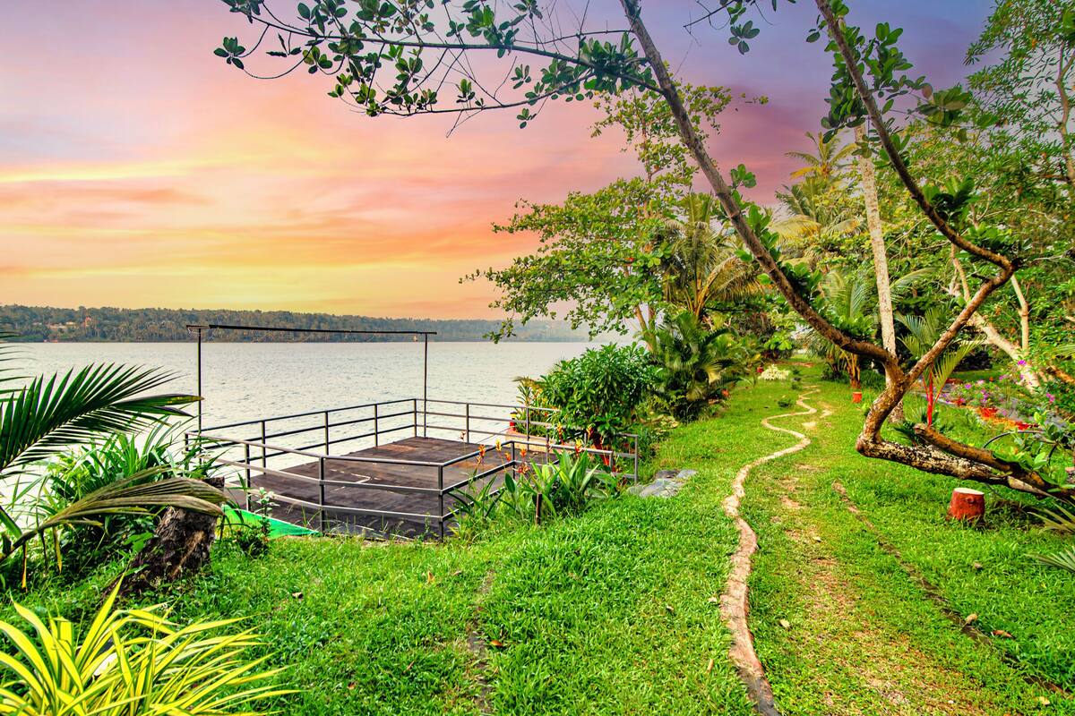 A garden with a wooden deck overlooking a lake, surrounded by lush greenery and a clear sky.