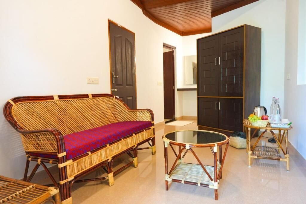 Una habitación con un sofá de mimbre, una mesa de centro de vidrio, un mueble de madera oscura y una mesita auxiliar de mimbre con frutas.