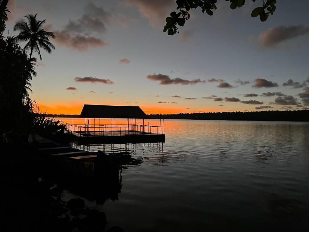 A dock extending into calm water with a sunset in the background.