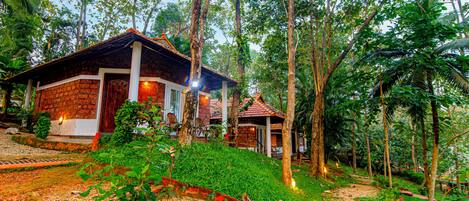 A rustic wooden house with a tiled roof, surrounded by lush greenery and trees.