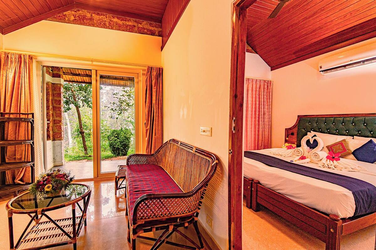 A hotel room with a bed, a seating area with a table, and a view of greenery outside.