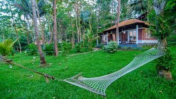 A hammock in a lush garden with a house in the background.
