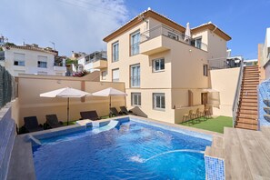 Une piscine avec des chaises longues et des parasols, un escalier et un bâtiment doté de balcons.