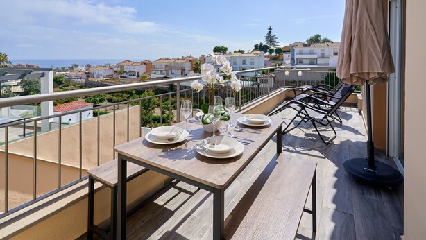 A balcony with a table set for dining, overlooking a coastal town. - Villa 'Oasis D Sol I-Private Pool' with Sea Views, Wi-Fi and Air Conditioning (Urbanización Cerro Garbancito)