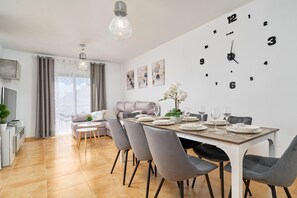 Een moderne eetruimte met een grote wandklok, grijze stoelen en een eettafel gedekt voor vier personen.