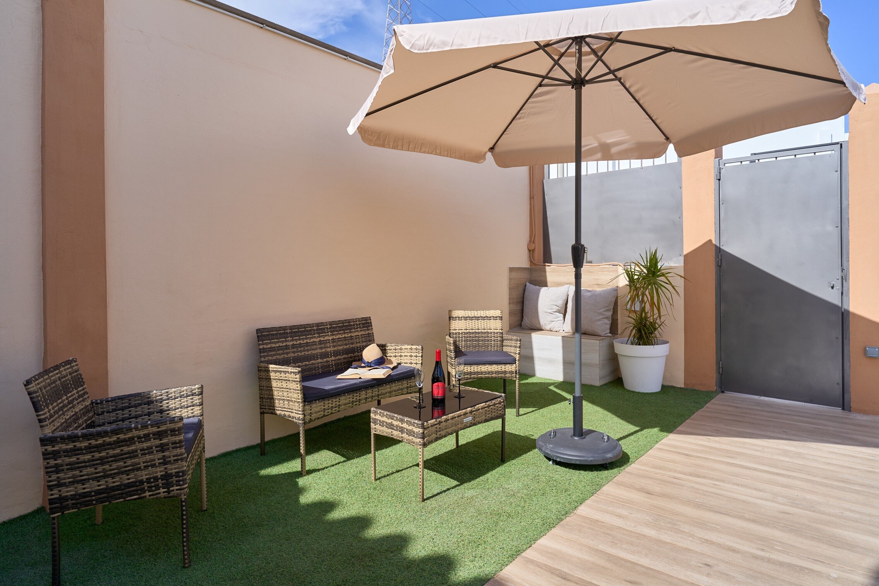 Un patio con muebles de mimbre, una mesa con una botella y una planta en maceta.