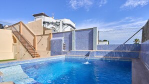 A swimming pool with a clear blue water, surrounded by a fence and a building with a white facade and a staircase. - Villa 'Oasis D Sol I-Private Pool' with Sea Views, Wi-Fi and Air Conditioning (Urbanización Cerro Garbancito)