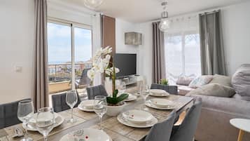 Spiseplads med et bord dækket til seks personer, en sofa og et fjernsyn i baggrunden.
