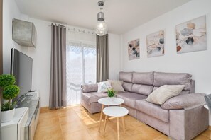 Un salon moderne avec un canapé, un téléviseur, une petite table et une plante en pot.