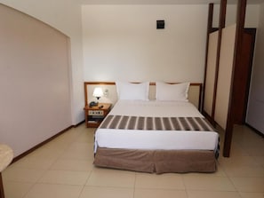 A hotel room with a large bed, a bedside table with a lamp, and a small cabinet. - Hotel beira rio (Itumbiara)