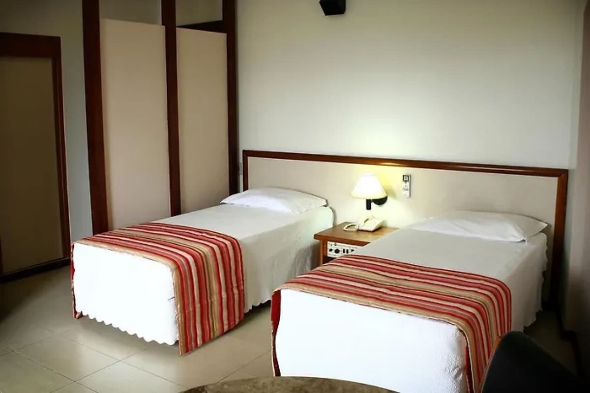 A hotel room with two single beds, a bedside table with a lamp, and a wall-mounted phone.