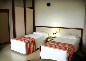 A hotel room with two single beds, a bedside table with a lamp, and a wall-mounted phone. - Hotel beira rio (Itumbiara)