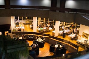 A spacious indoor dining area with multiple tables and chairs, a central seating area with round tables, and a high ceiling with visible structural beams. - Hotel beira rio (Itumbiara)