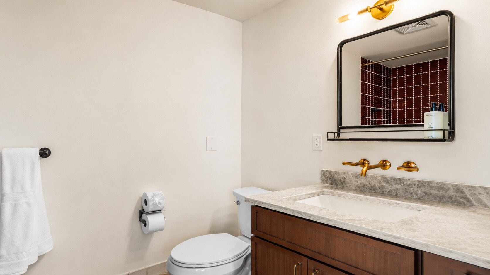 A bathroom with a toilet, sink, mirror, and towel rack.