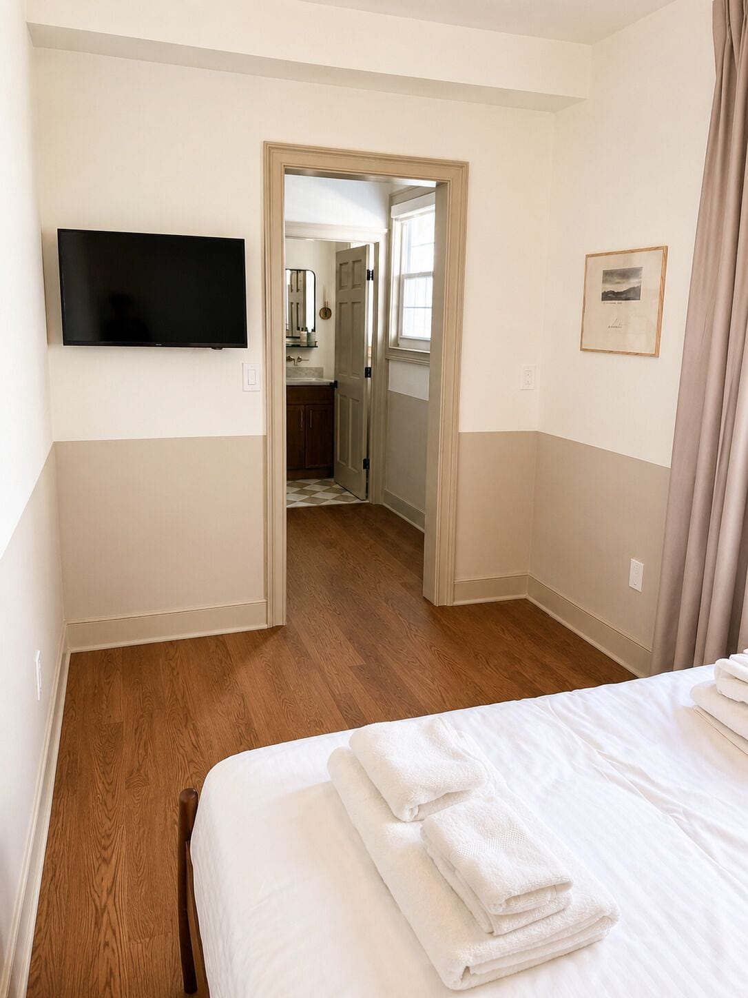 Una habitación de hotel con una cama, un televisor de pantalla plana, un cuadro en la pared y vistas al área de la cocina contigua.
