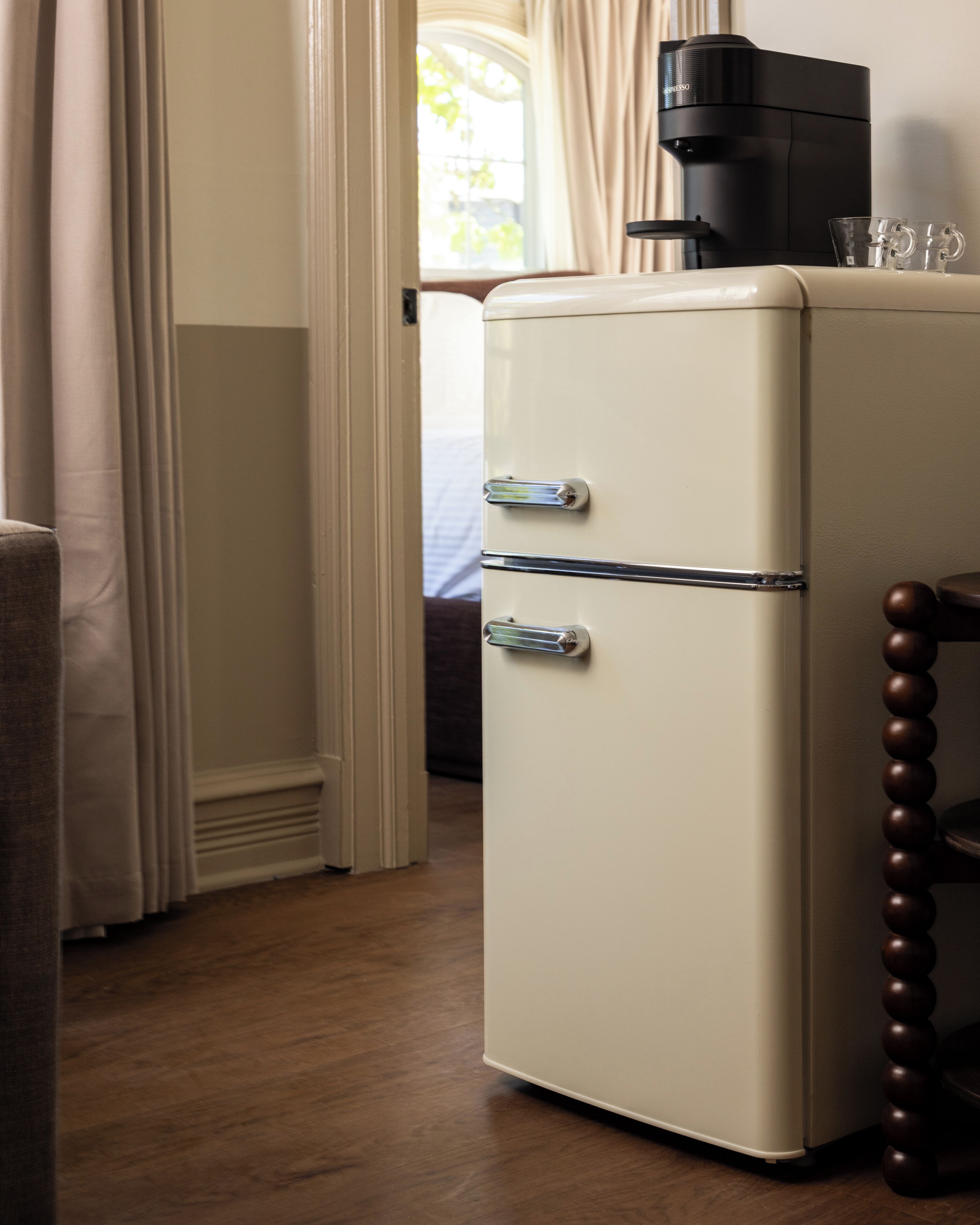 Un refrigerador antiguo con dos cajones, una cafetera encima y una silla de madera con respaldo redondo.