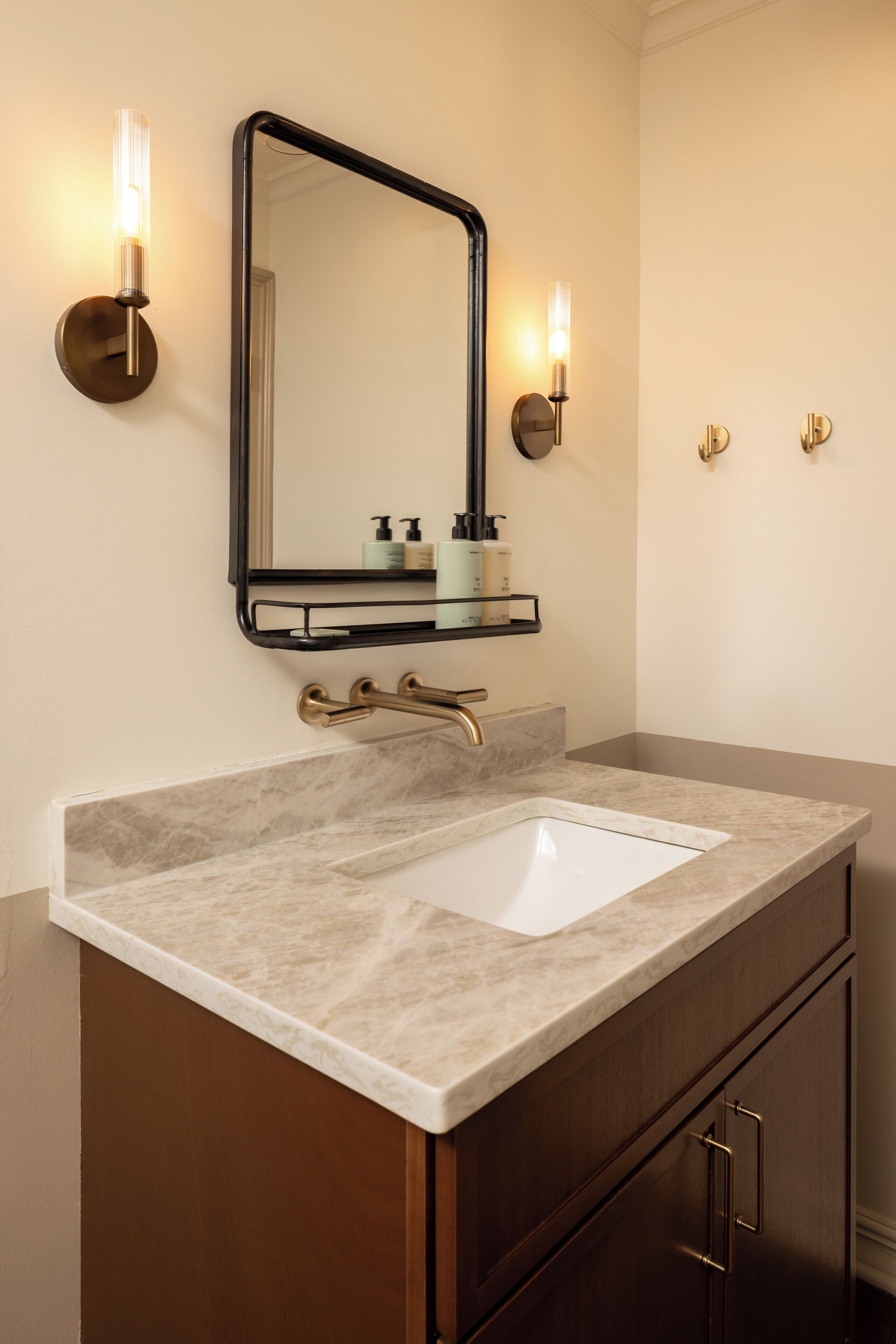 A bathroom with a marble sink, a black-framed mirror, and wall-mounted sconces.