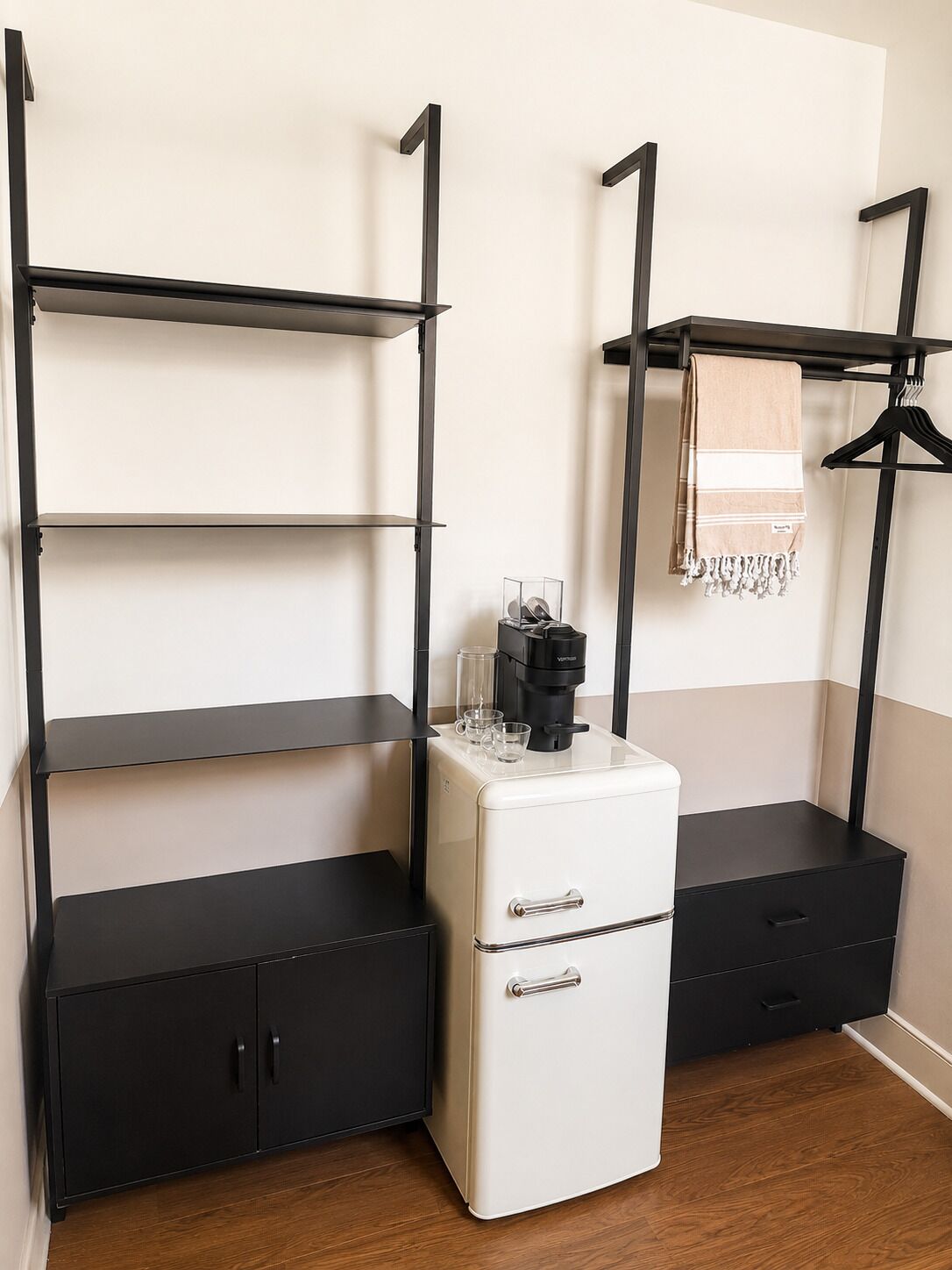 Eine kleine Küchenzeile mit einem weißen Kühlschrank, schwarzen Schränken und einer Kaffeemaschine auf der Arbeitsplatte.