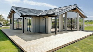 Ein modernes Haus mit geneigtem Dach, großen Glasfenstern und einer Holzterrasse.