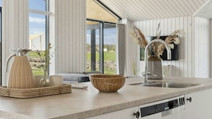 Eine Küche mit einem großen Fenster, einem Spülbecken, einer Vase mit getrockneten Blumen und einem Korbkörbchen auf der Arbeitsfläche.