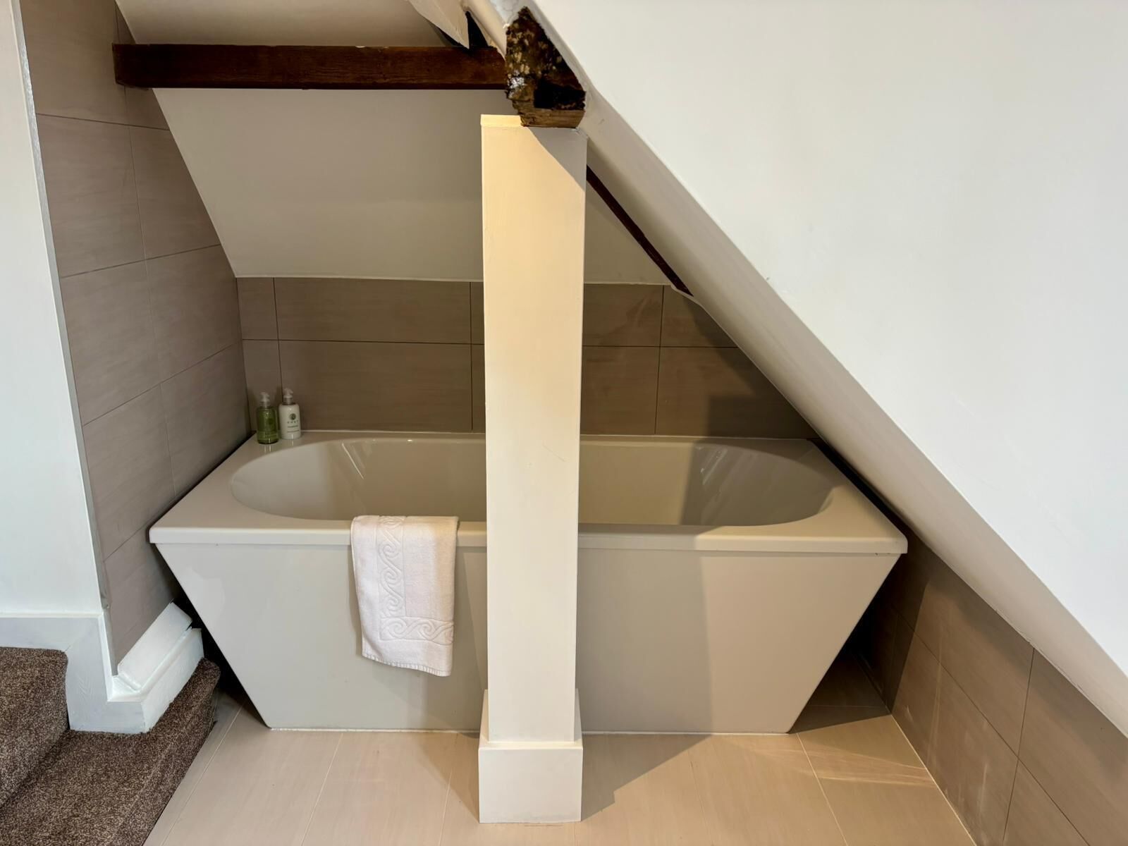 A modern bathroom with a freestanding bathtub, a towel hanging on the wall, and a wooden beam above.