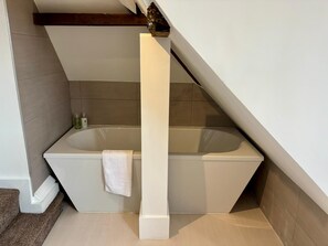 A modern bathroom with a freestanding bathtub, a towel hanging on the wall, and a wooden beam above. - Horse & Farrier Carlisle (Carlisle)