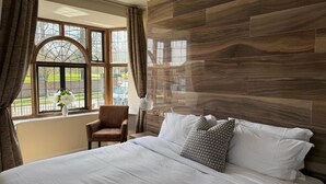 Un dormitorio con una cama grande, una silla, una ventana con cortinas y vistas a la vegetación exterior.