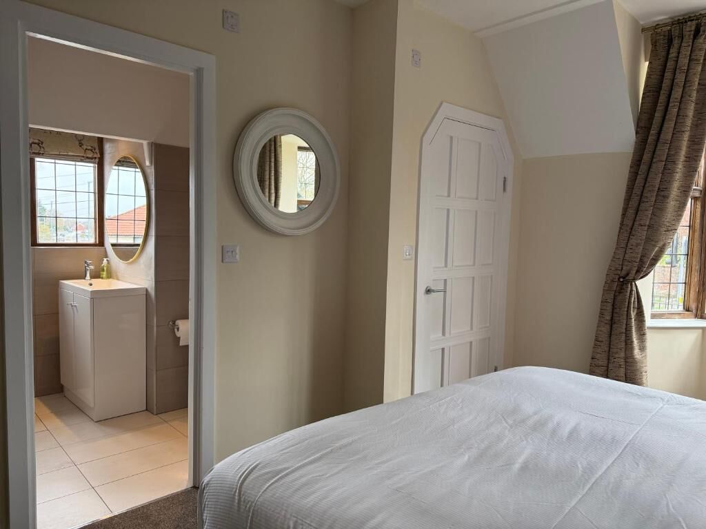 Un dormitorio con cama, una puerta, un espejo y un baño a la vista a través de una puerta abierta.