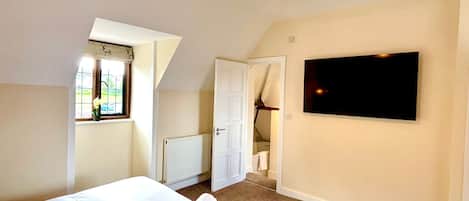 A bedroom with a bed, a TV mounted on the wall, a window with a view, and a ceiling light fixture.