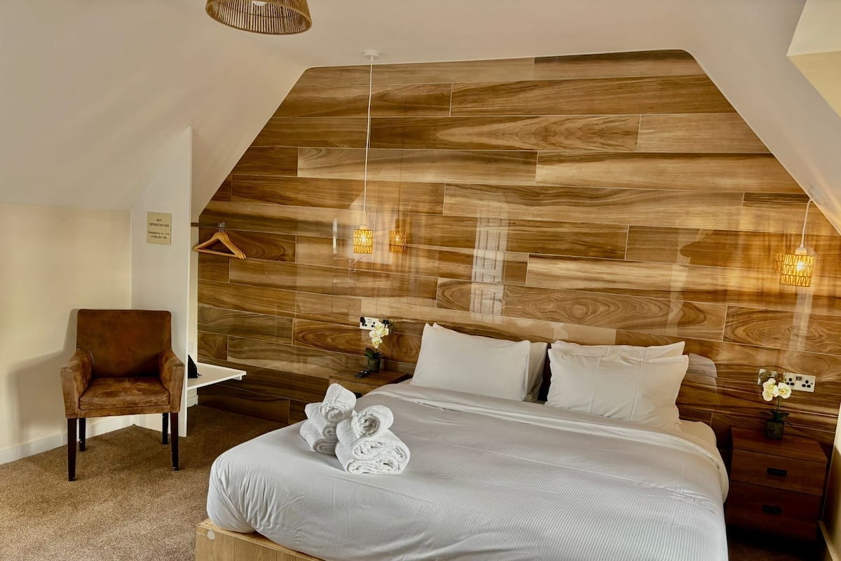 A bedroom with a wooden headboard, a bed with white linens, a chair, and a small table with a plant.